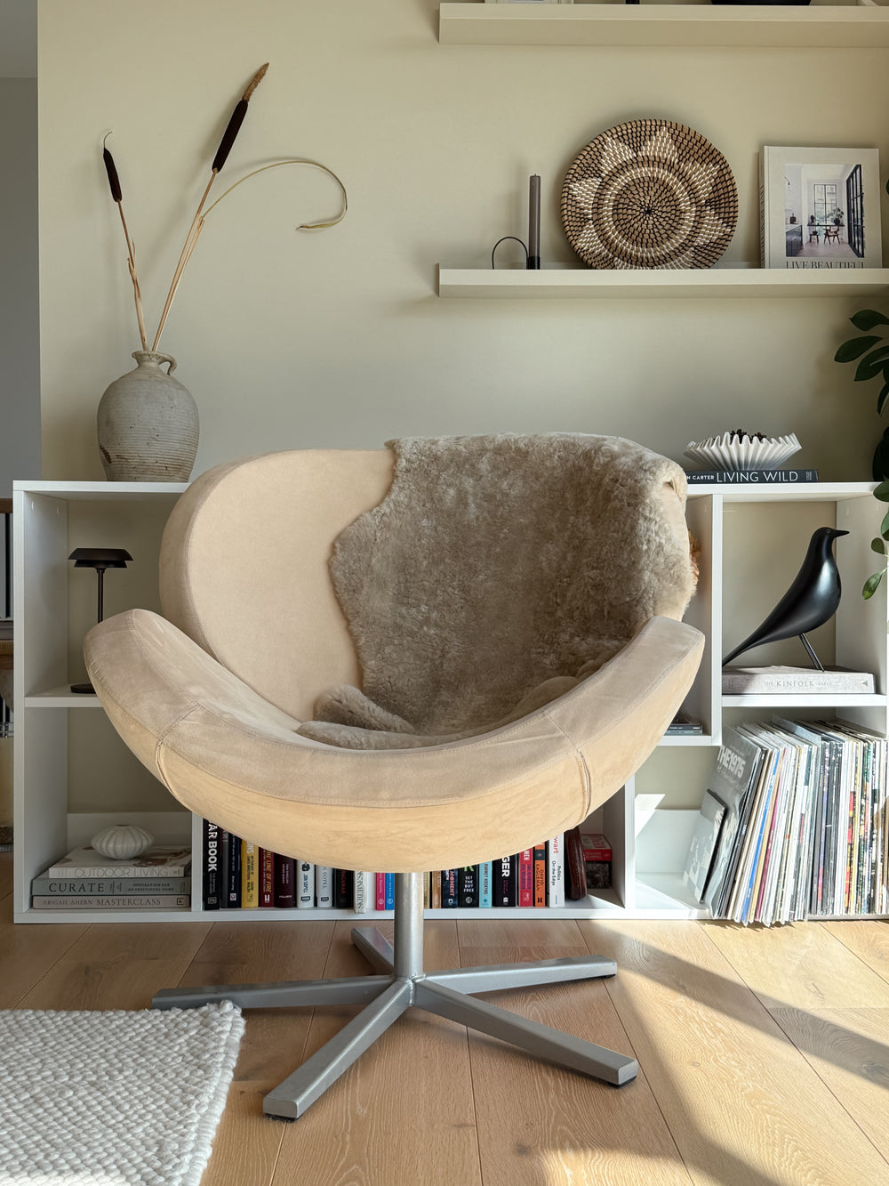 Beige chair with a brown cushion in a room with bookshelves and decorative items.