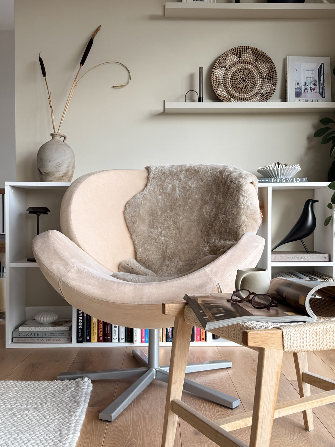 Modern interior with a beige chair, wooden table, and shelves with decor items.
