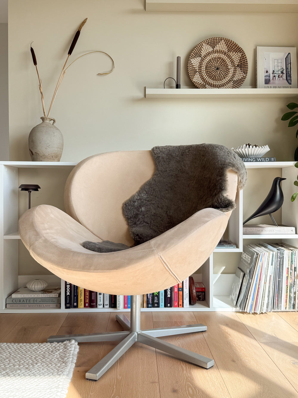 Beige armchair with a dark gray cushion in a room with bookshelves and decorative items.